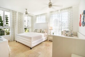 Ein Schlafzimmer mit Bett, Nachttischen, einer Lampe, Vorhängen und Blick auf Grünflächen.