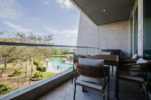 A balcony with wicker furniture, a view of a swimming pool, and a modern building with white brick walls. - 2-br Sea Pool View Apartment Pet-friendly (Cartagena)