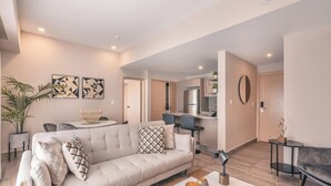 A modern living room with a sofa, dining table, and chairs, a kitchen area, and a hallway leading to a bedroom. - Flat in Regatta Ii 204 (Santo Domingo)