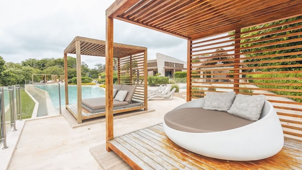 Un espacio al aire libre moderno con piscina, una pérgola de madera y una silla de descanso.
