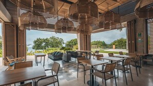 Un área de comedor al aire libre con mobiliario de mimbre, vistas al océano y un diseño arquitectónico moderno.