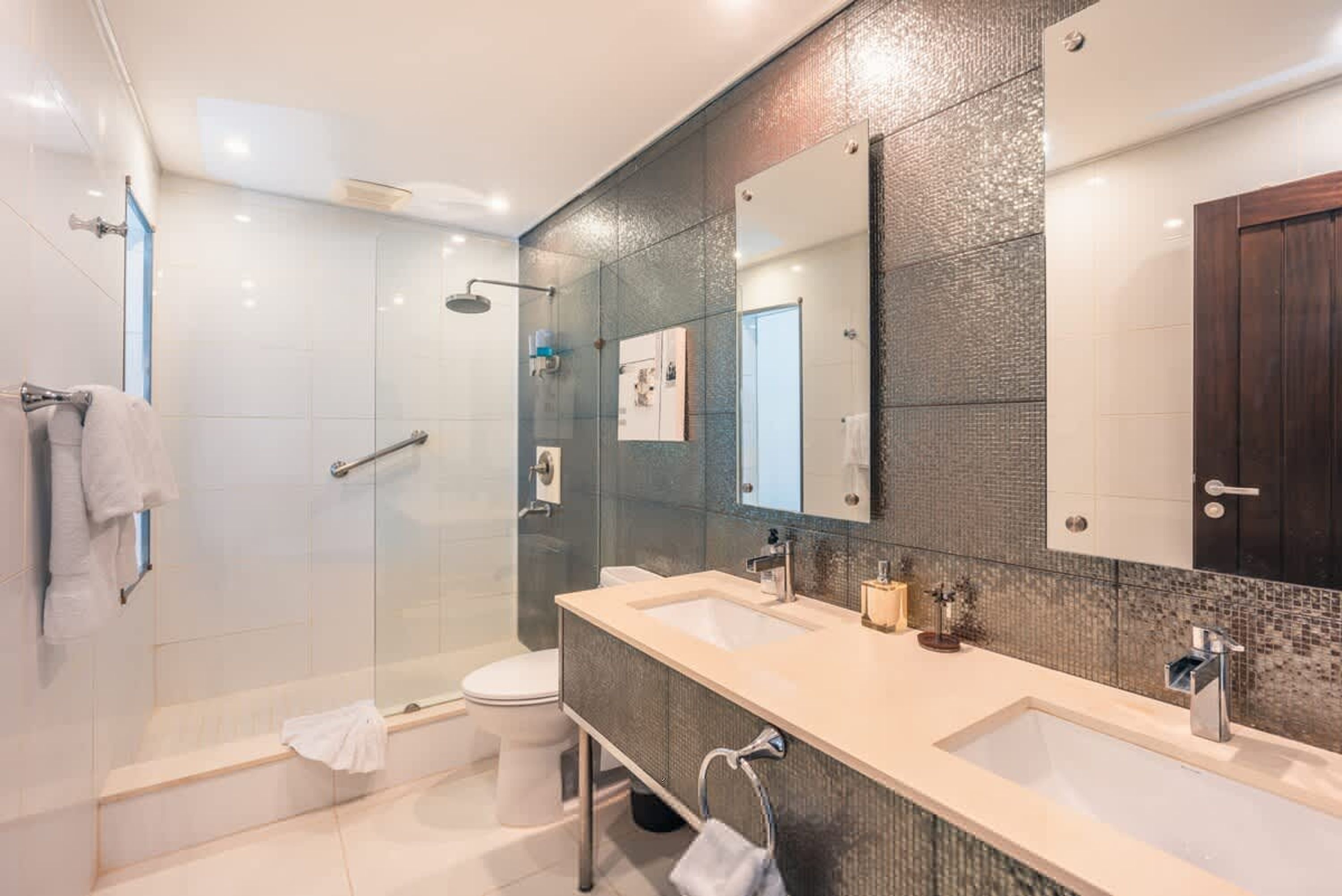 Un baño moderno con cabina de ducha de vidrio, tocador doble y un espejo grande.