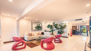 Un salon moderne avec un canapé, deux fauteuils rouges, une table basse et une grande plante en pot.