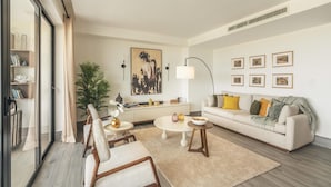 A modern living room with a sofa, coffee table, chairs, a plant, and artwork on the walls.
