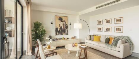 Una sala de estar moderna con sofá, mesa de centro, sillas, una planta y obras de arte en las paredes.