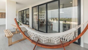 A hammock in a modern room with large windows, a wooden bench, and a view of the outdoors.