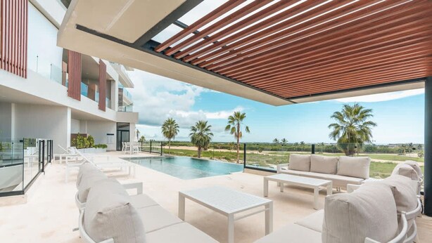 A modern outdoor lounge area with a pool, seating, and a view of palm trees and the ocean.
