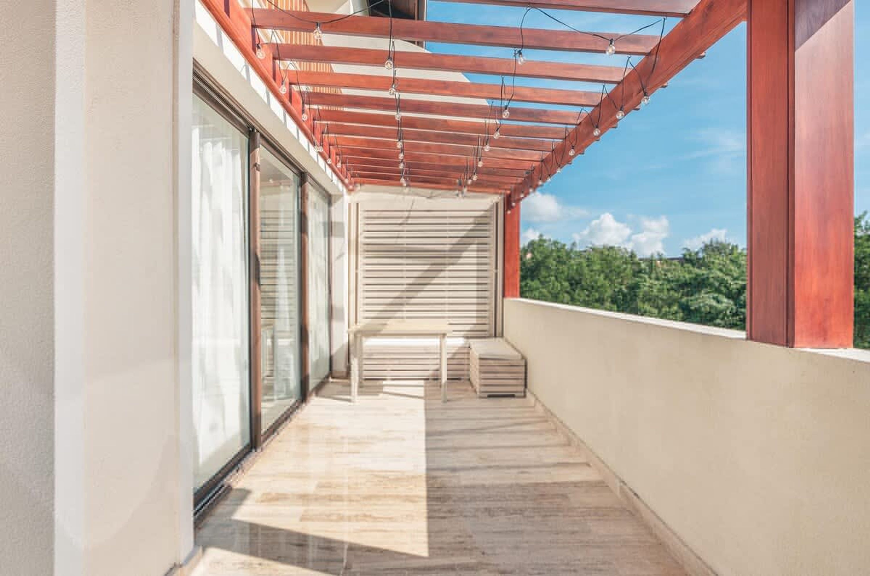 Ein Balkon mit einer Holz-Pergola, einer Schiebeglastür und Blick ins Grüne.