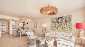 A modern living room with a white sofa, round ottomans, a dining area with chairs, a kitchen in the background, and a large abstract painting on the wall. - 2 Br 6 Guests Nearby Beach Portillo (Las Terrenas)