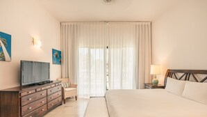 A hotel room with a bed, a TV, a dresser, a lamp, and a window with curtains. - 2br Apt 5 Guests Balcony With Pool View (Las Terrenas)