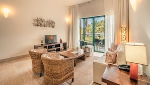 A living room with wicker furniture, a TV, a lamp, and a view of a balcony with palm trees. - 2br Apt 5 Guests Balcony With Pool View (Las Terrenas)
