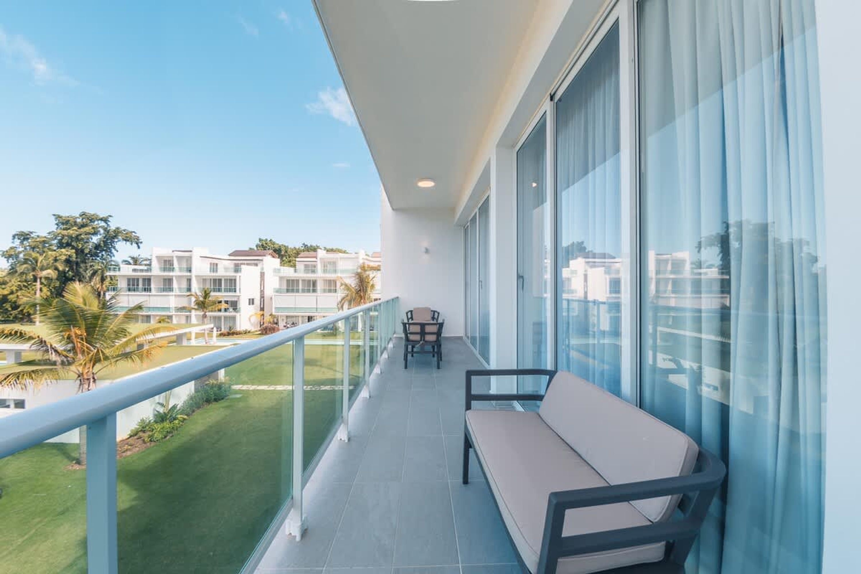 Un balcon doté d’un canapé, d’une chaise et d’une balustrade, offrant une vue sur une pelouse bien entretenue et d’autres bâtiments.