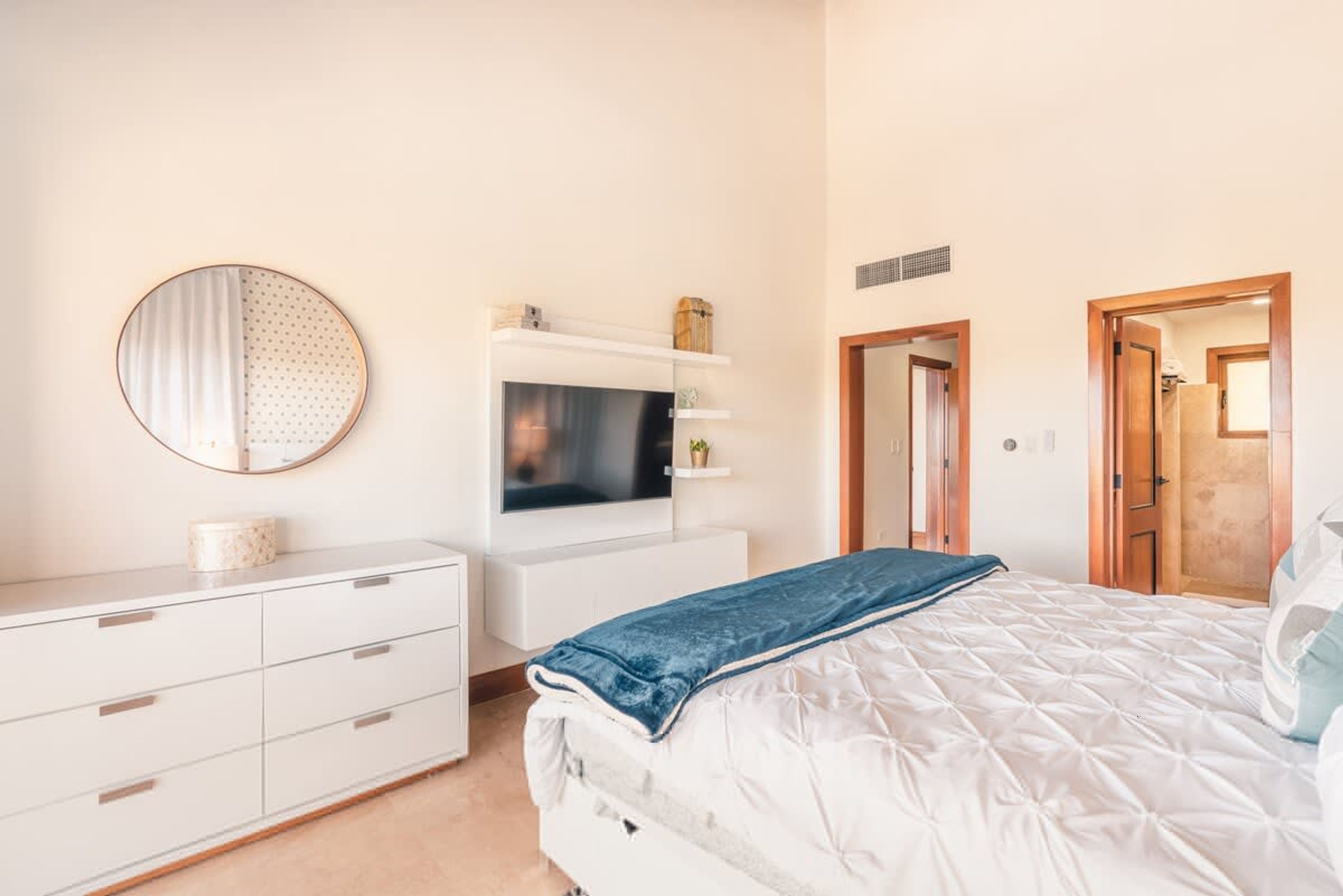 A bedroom with a bed, a TV, a dresser, a mirror, and a door.