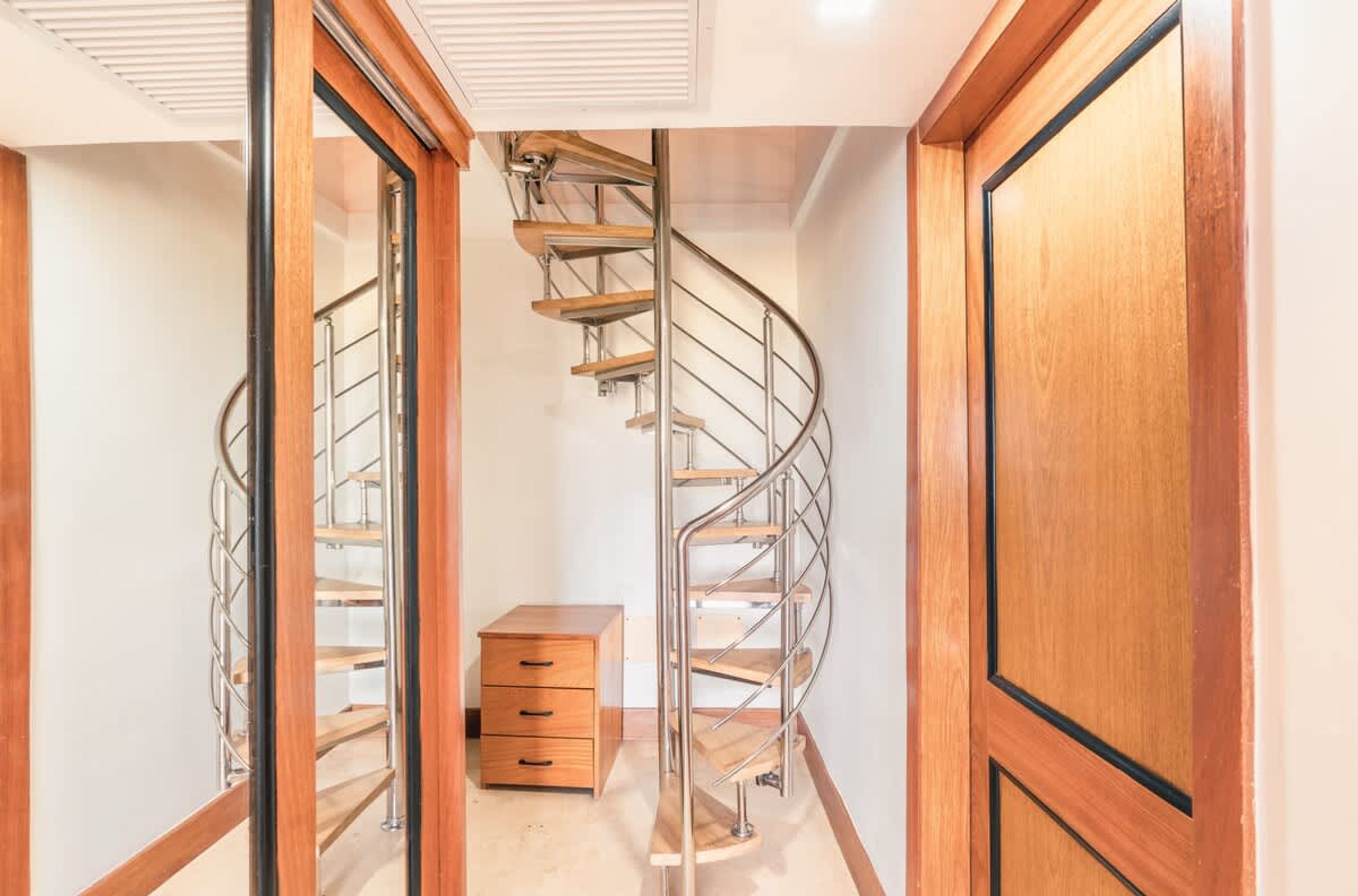 A spiral staircase with metal railings, a wooden drawer unit, and a wooden door.