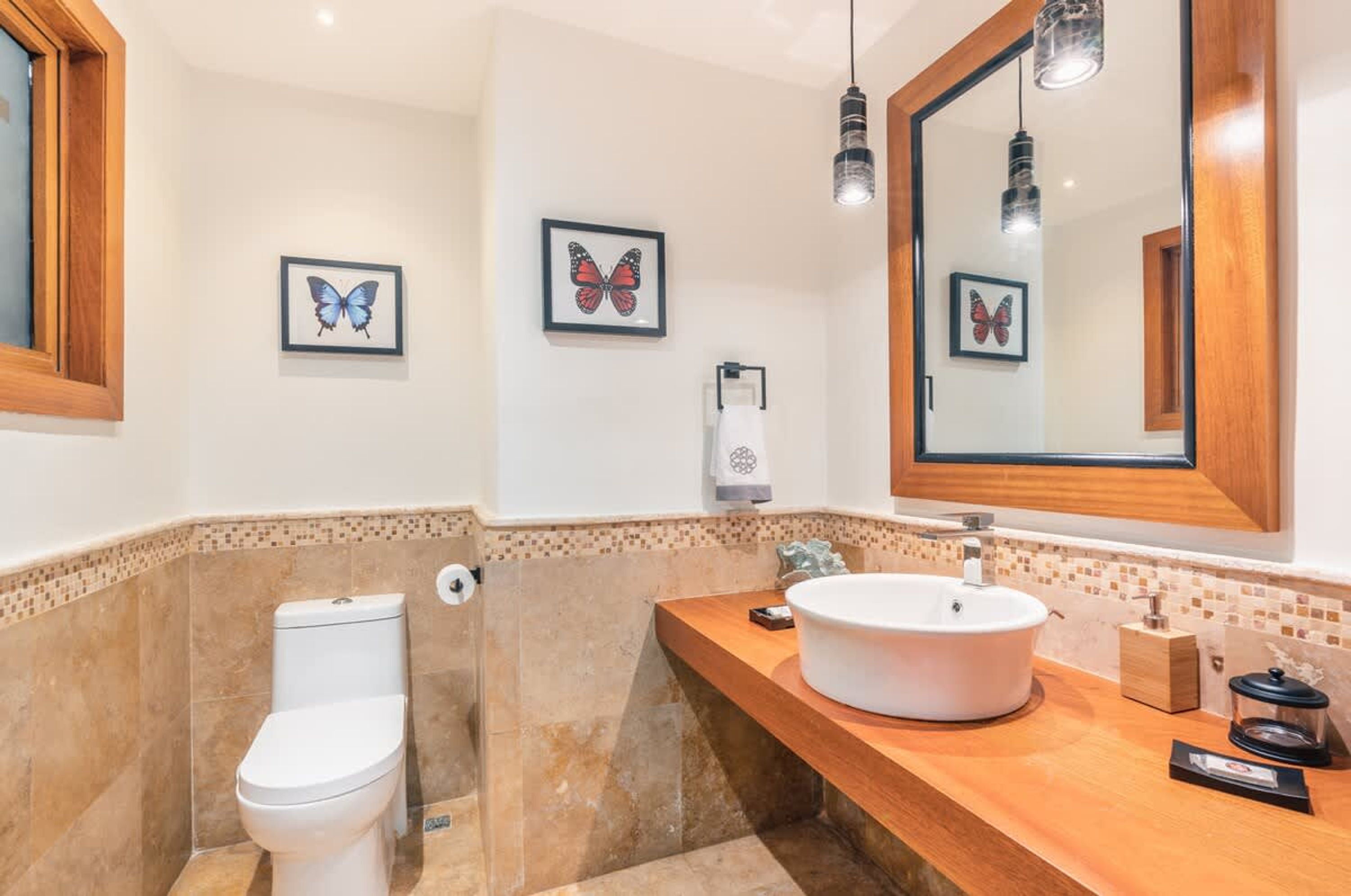 A bathroom with a toilet, sink, and mirror. There are butterfly wall art pieces and a towel dispenser.