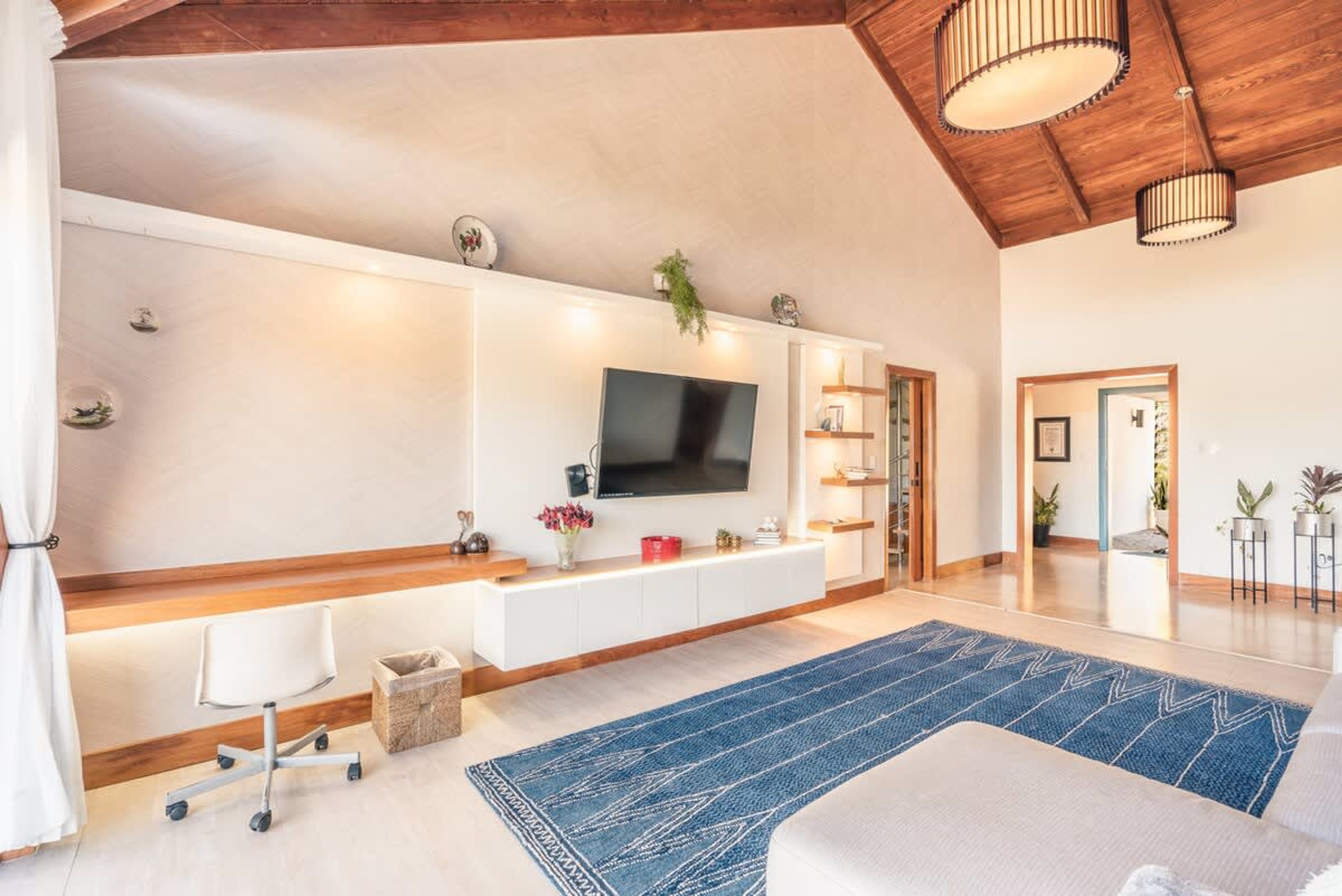 Un salon moderne doté d’un téléviseur à écran plat, de meubles blancs, d’un tapis bleu et d’un plafond en bois.