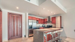 A modern kitchen with a central island, stainless steel appliances, and red cabinetry. - Apartment few Steps to the Beach at Punta Palmera (Punta Cana)