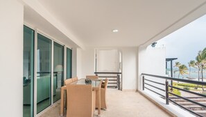 Ein Balkon mit Tisch, Stühlen, Glastüren und Blick auf den Ozean.
