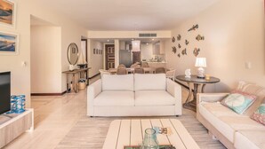 Ein Wohnzimmer mit einer Couch, einem Couchtisch und einem Fernseher. Es gibt einen Essbereich mit Stühlen und einem Tisch.