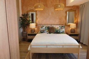 Quarto com cama, duas luminárias de cabeceira, um espelho, uma planta em vaso e uma mesinha de cabeceira de madeira.
