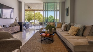 A modern living room with a sofa, coffee table, and a large window offering a view of greenery. - 3br-apt 6 Guests Jacuzzi Calablanca (Cartagena)