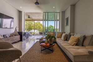 A modern living room with a sofa, coffee table, and a large window offering a view of greenery. - 3br-apt 6 Guests Jacuzzi Calablanca (Cartagena)