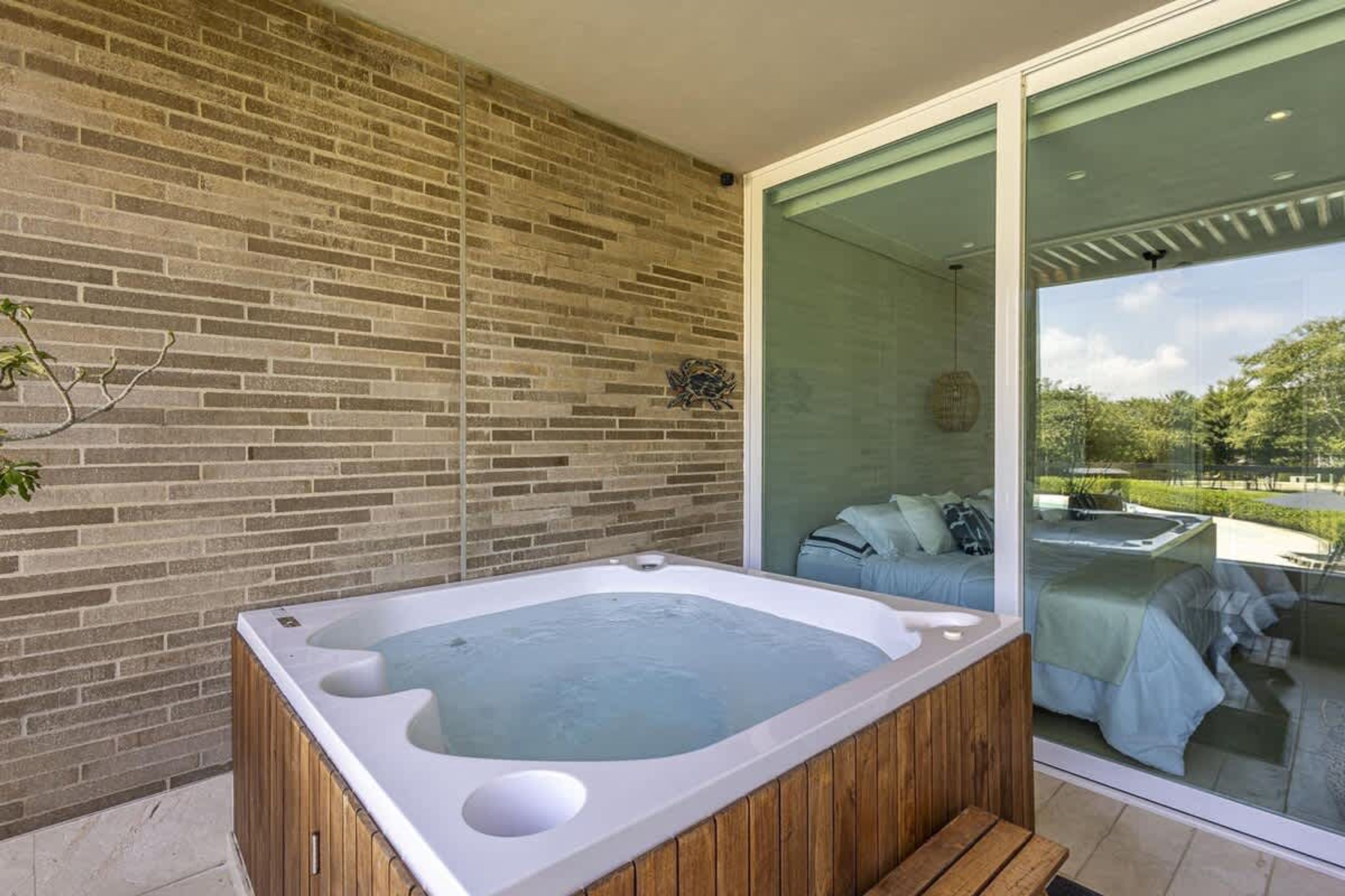 Un bain à remous extérieur moderne, doté d’une structure en bois, d’un mur en briques et d’une porte en verre donnant sur un espace patio.