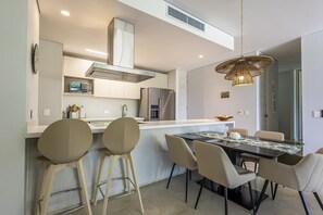 Una cocina moderna con una isla central, taburetes de bar y una mesa de comedor con sillas.