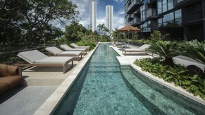 Ein Poolbereich mit Liegestühlen, einem klaren Pool und modernen Gebäuden im Hintergrund.