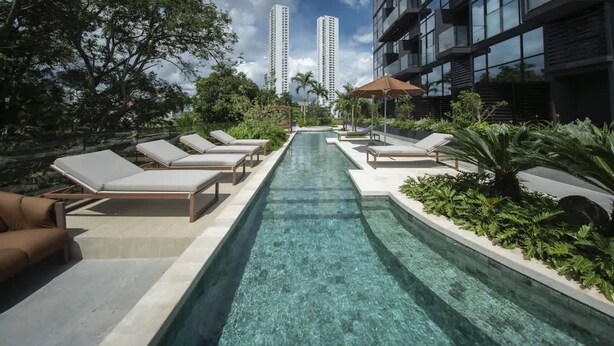 A pool area with lounge chairs, a clear pool, and modern buildings in the background. - Loft-style 1br Apt At Coco del mar (Panama City)