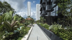 A pathway lined with greenery, a small pavilion, and tall buildings in the background. - Loft-style 1br Apt At Coco del mar (Panama City)