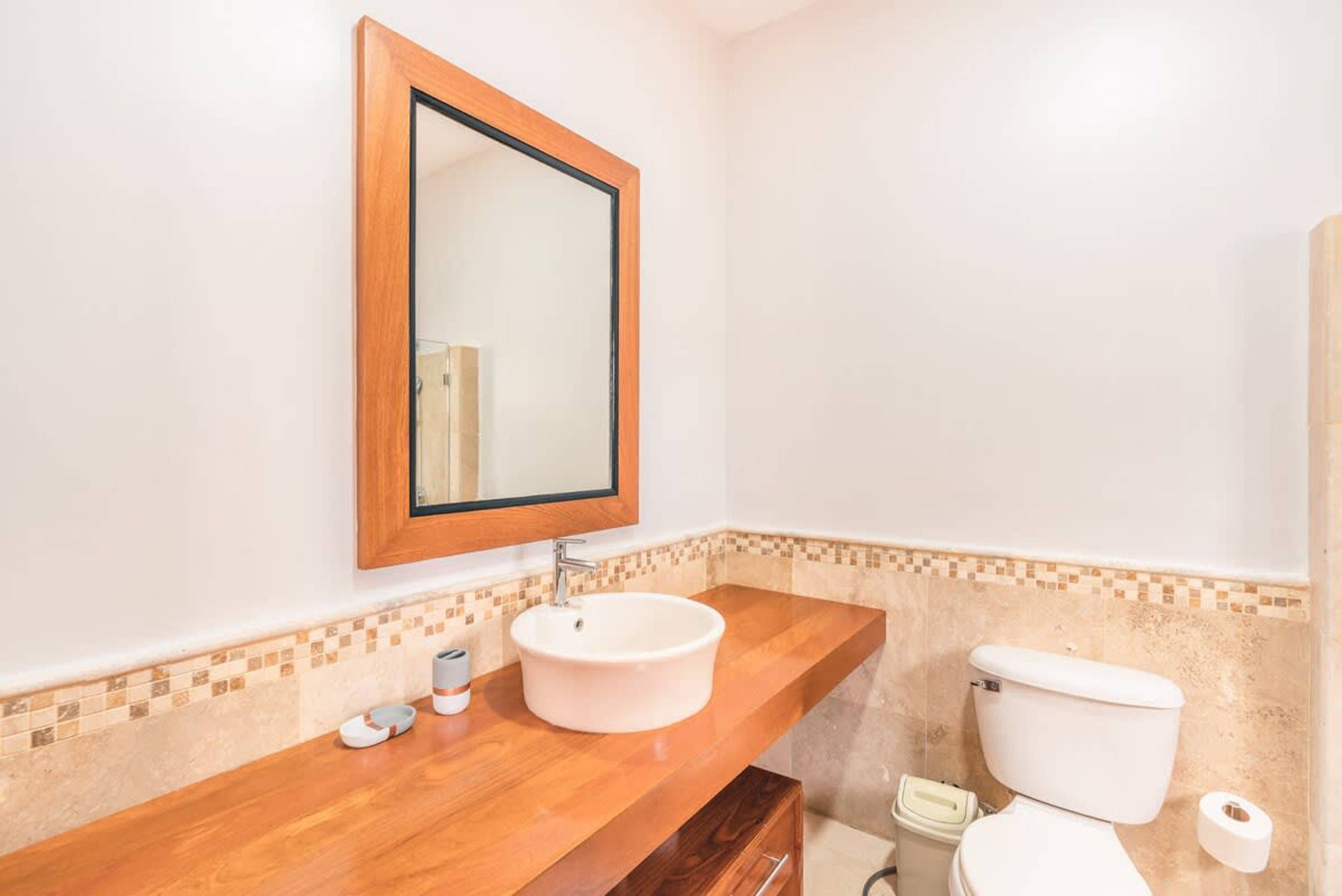 Ein Badezimmer mit einem Holzkosmetikschrank, einem weißen Waschbecken, einem Spiegel, einer Toilette und einer kleinen Mülltonne.
