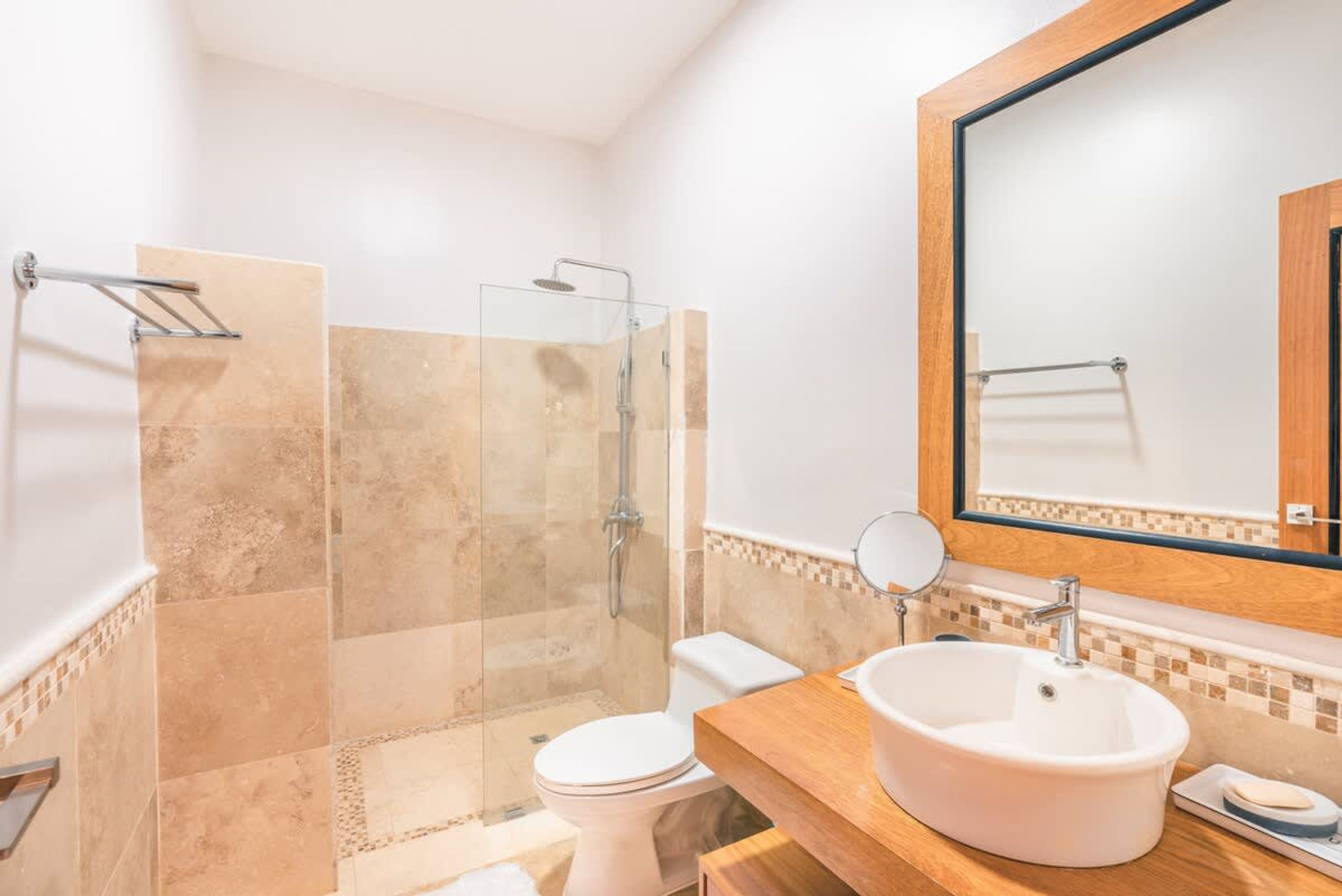 A bathroom with a glass-enclosed shower, a white toilet, a wooden vanity with a sink, and a mirror.