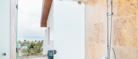A bathroom with a shower, a glass door leading to a balcony with a view of the ocean.