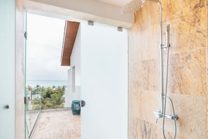 A bathroom with a shower, a glass door leading to a balcony with a view of the ocean.