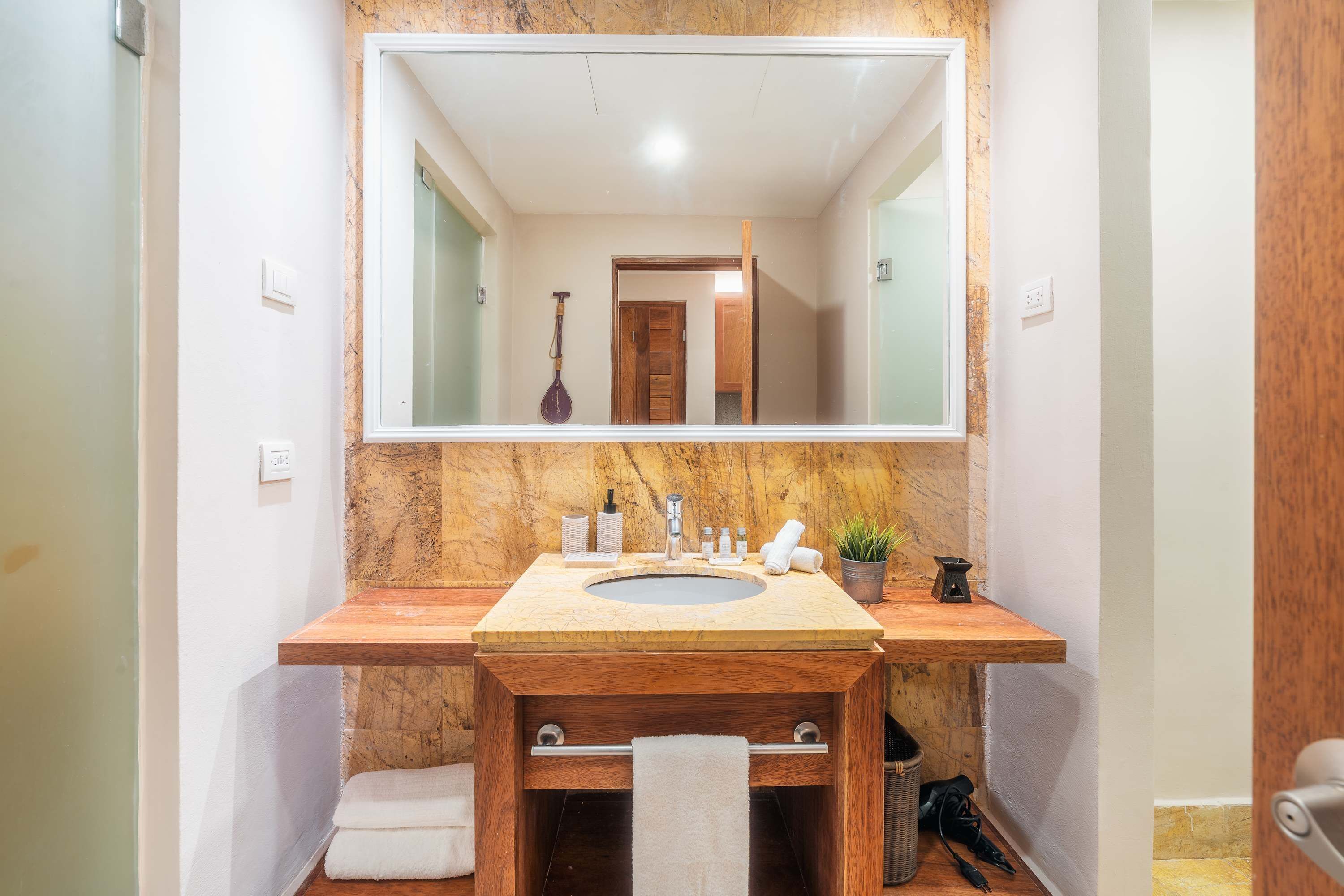 Een badkamer met een marmeren aanrechtblad, een grote spiegel, een houten wastafelmeubel, een wastafel en een handdoekhouder.