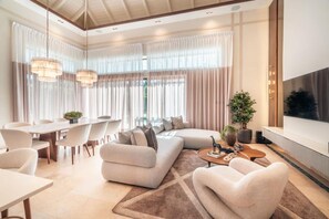 A modern living room with a sectional sofa, a dining area with a white table and chairs, and a large TV mounted on the wall. - Incredible 3br Bungallow With Patio and Pool (Punta Cana)
