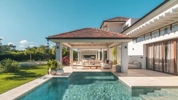 Una casa moderna con piscina, patio cubierto y un jardín bien cuidado.