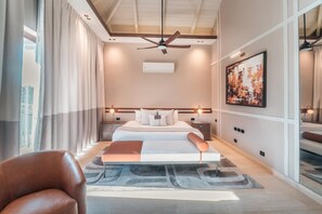 A modern hotel room with a large bed, a ceiling fan, an air conditioner, a painting, and a view of the city. - Incredible 3br Bungallow With Patio and Pool (Punta Cana)