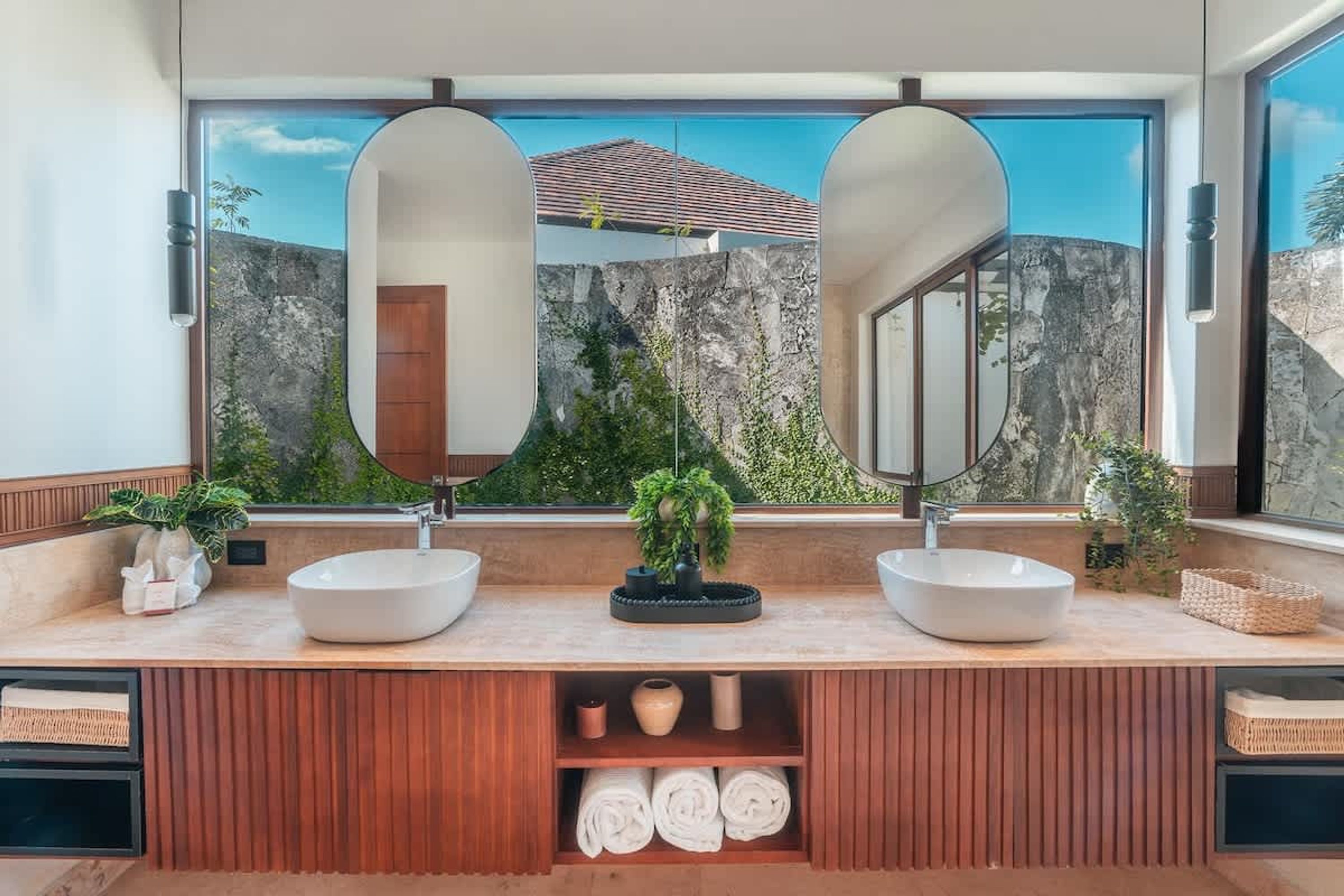 Casa de banho moderna com duas grandes espelhas, toucador de madeira e vista para terreno rochoso.