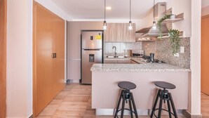 Moderni keittiö, jossa on keskeinen saareke, baarituolit, riippuvalaisimet ja sisäänrakennettu liesi.