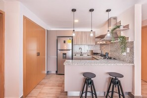 A modern kitchen with a central island, bar stools, pendant lighting, and a built-in stove. - Flat in Piantini 304 (Santo Domingo)