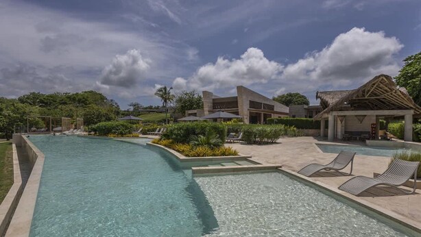 Una piscina con sillones reclinables, una zona cubierta y un edificio con una estructura de techo distintiva.