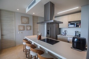 A modern kitchen with a central island, bar stools, a built-in oven, and a coffee machine.
