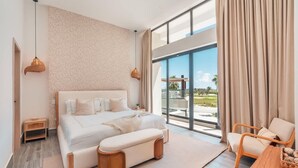 Un dormitorio moderno con una cama grande, una mesita de madera, un banco de mimbre y vistas al exterior a través de amplias ventanas.
