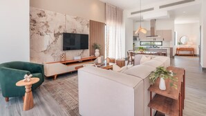 Una sala de estar moderna con un televisor de pantalla plana grande, un sillón verde, un sofá beige y una mesa de centro de madera.