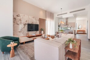 A modern living room with a large flat-screen TV, a green armchair, a beige sofa, and a wooden coffee table. - New Loft With 2br and Golf View in Cap Cana (Punta Cana)