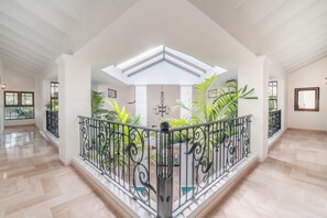 A spacious interior with a high ceiling, a central open area with plants, and a balcony with ornate railing. - Majestic Villa 6br 16 Ppl Private Pool Maid (La Romana)