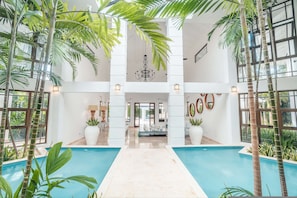 An indoor swimming pool with a central walkway, surrounded by tall palm trees and potted plants. - Majestic Villa 6br 16 Ppl Private Pool Maid (La Romana)