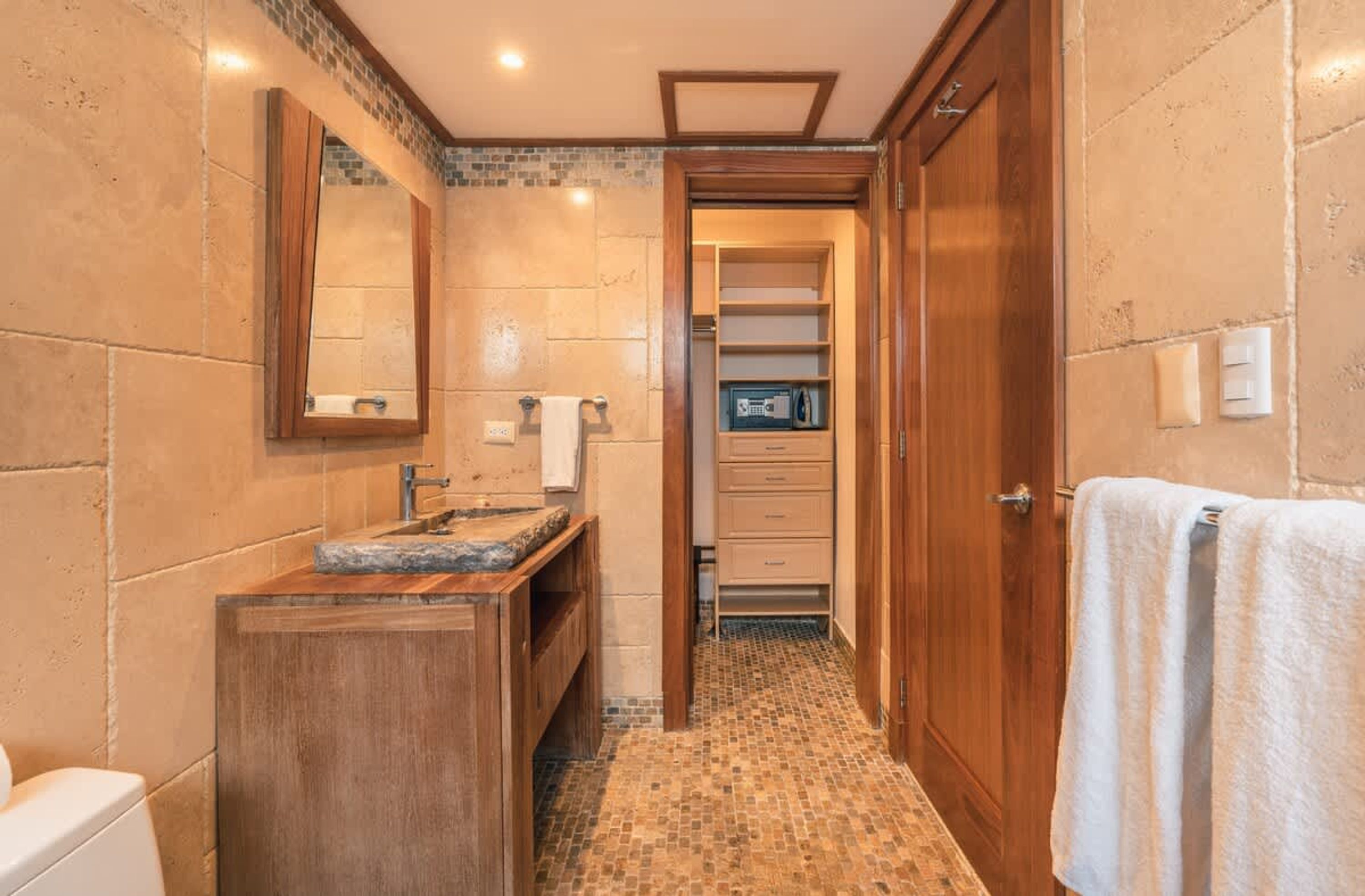 Un bagno con un mobile bagno in legno, uno specchio, un portascopevoli e un pavimento piastrellato.